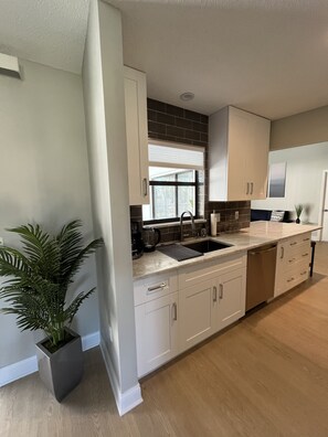A modern kitchen with white cabinets, a black backsplash, and a large window.