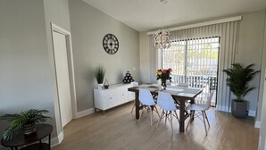 A spacious living room with a dining area, a white sofa, a dining table with chairs, and a large window with curtains. - Home in Englewood / heated pool (Englewood)