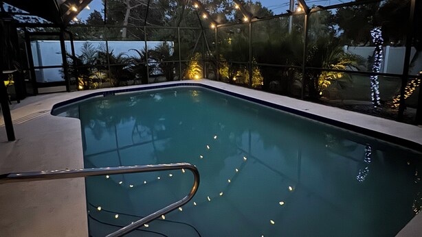 A swimming pool with a glass enclosure, surrounded by trees and string lights. - Home in Englewood / heated pool (Englewood)