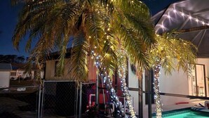 A palm tree decorated with string lights, a swimming pool, and a covered outdoor area. - Home in Englewood / heated pool (Englewood)