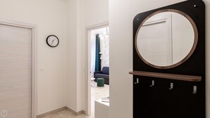 Un pasillo con una puerta, un reloj y un espejo con ganchos.