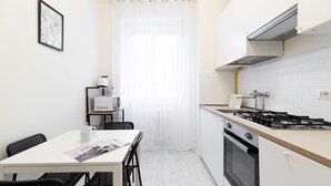 Una cocina compacta con estufa a gas, horno y microondas. Cuenta con una mesa de comedor con sillas y un mueble pequeño con una tetera.