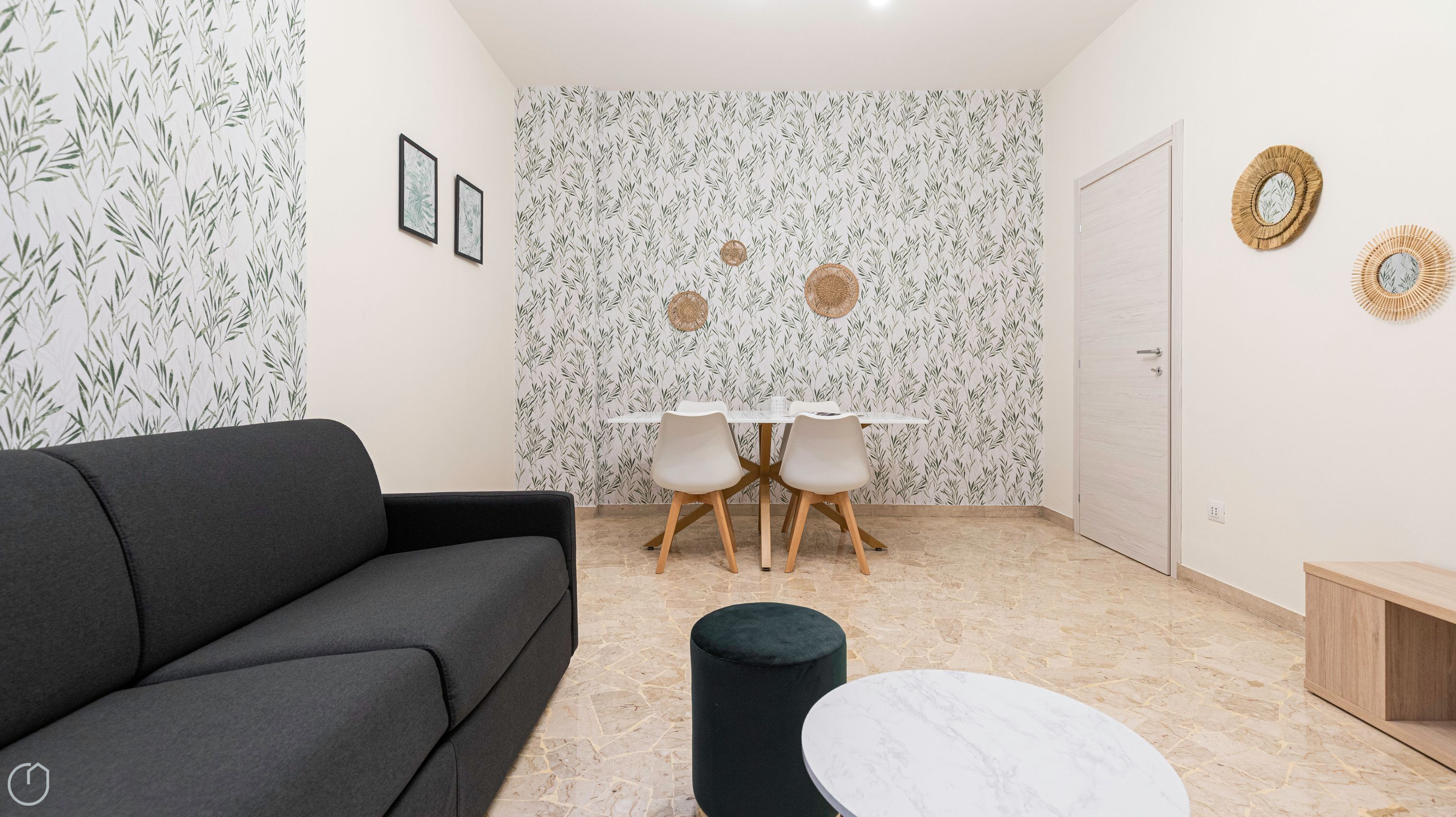Una sala de estar moderna con un sofá gris, una mesa de centro de mármol redonda y un comedor con una mesa blanca y dos sillas.