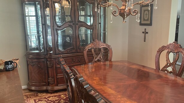 Une salle à manger avec une grande table en bois, des chaises décorées, un meuble vitré et un lustre.