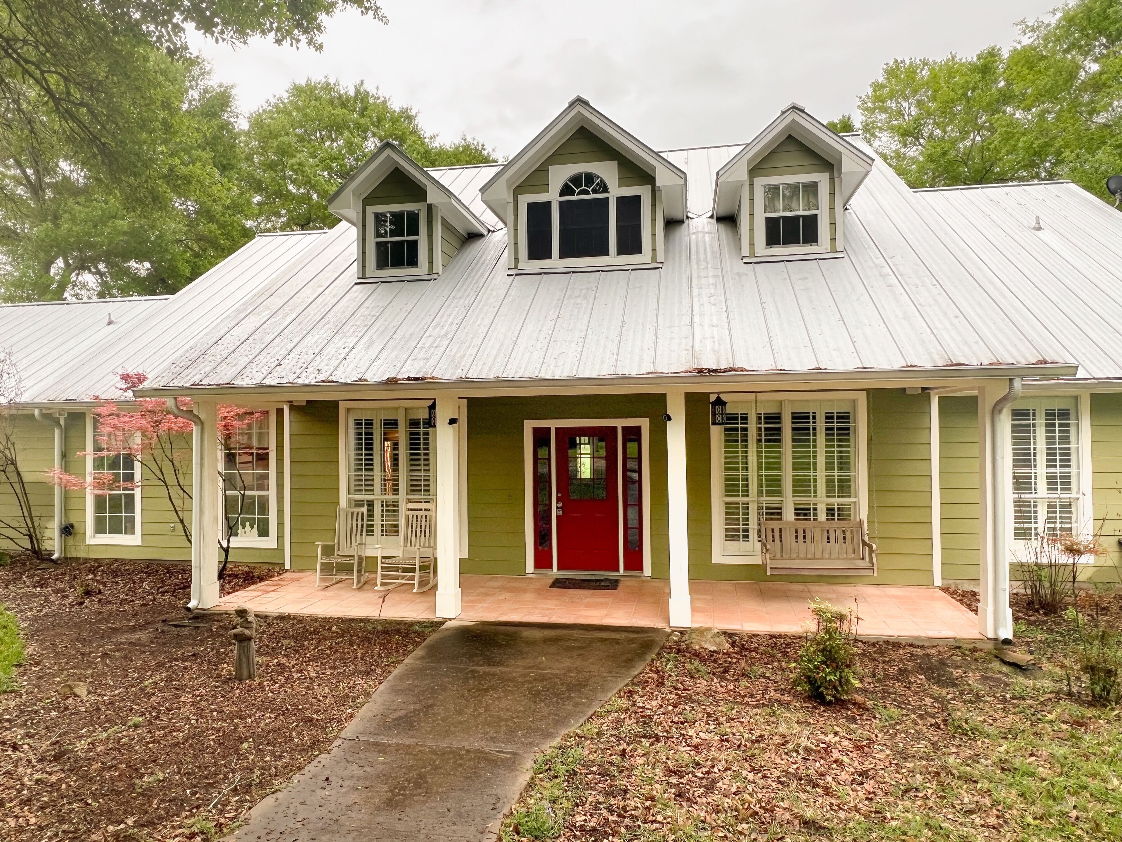 A two-story house with a red door, a covered porch, and a metal roof.