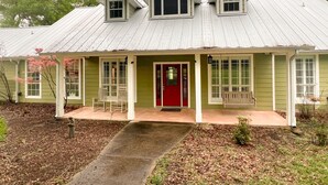 Une maison à deux étages avec une porte rouge, un porche couvert et un toit en métal.