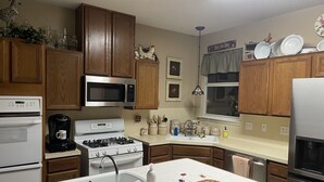Une cuisine avec des meubles de rangement en bois, un four à micro-ondes, une cuisinière et divers ustensiles de cuisine sur le plan de travail.