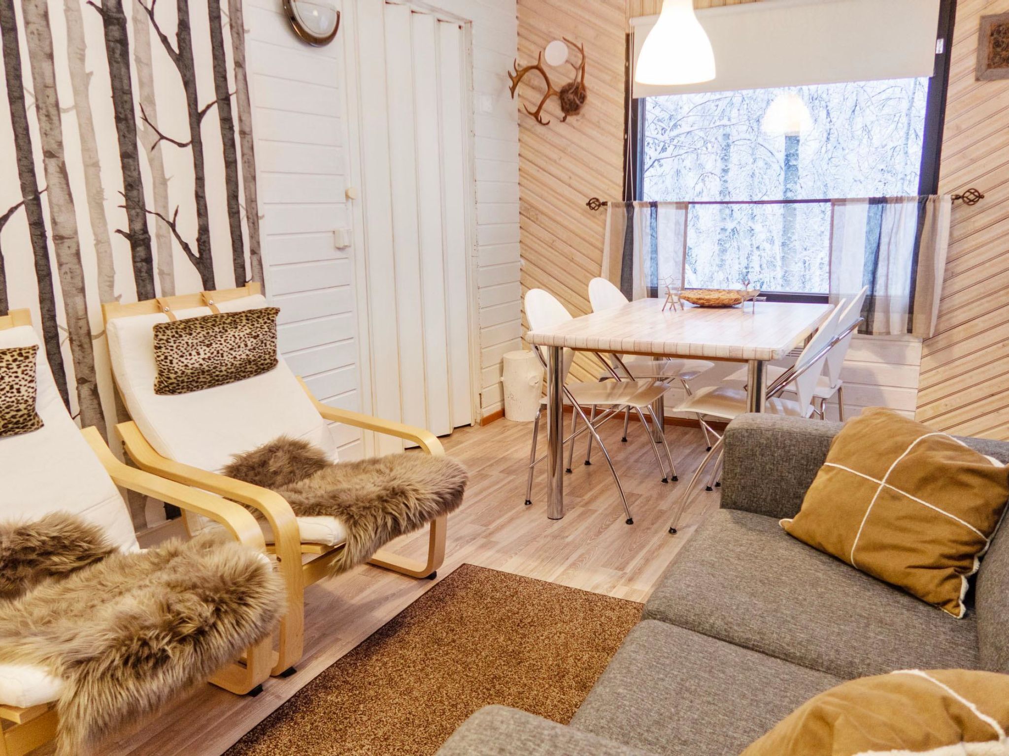A cozy room with a wooden floor, a dining table with chairs, a sofa, and a chair with a fur throw.
