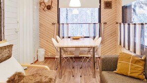 A cozy room with a wooden floor, a dining table with chairs, a sofa, and a window with a view of trees.