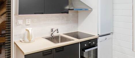 Eine moderne Küche mit schwarzen Schränken, einer Edelstahl-Spüle, einem eingebauten Backofen und einem weißen Kühlschrank.