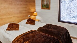 A bedroom with two beds, a nightstand, a lamp, a window with a snowy view, and a painting on the wall.