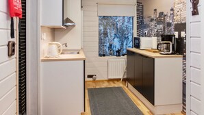 A compact kitchen with a microwave, coffee maker, and kettle. A window with a snowy forest view is visible.