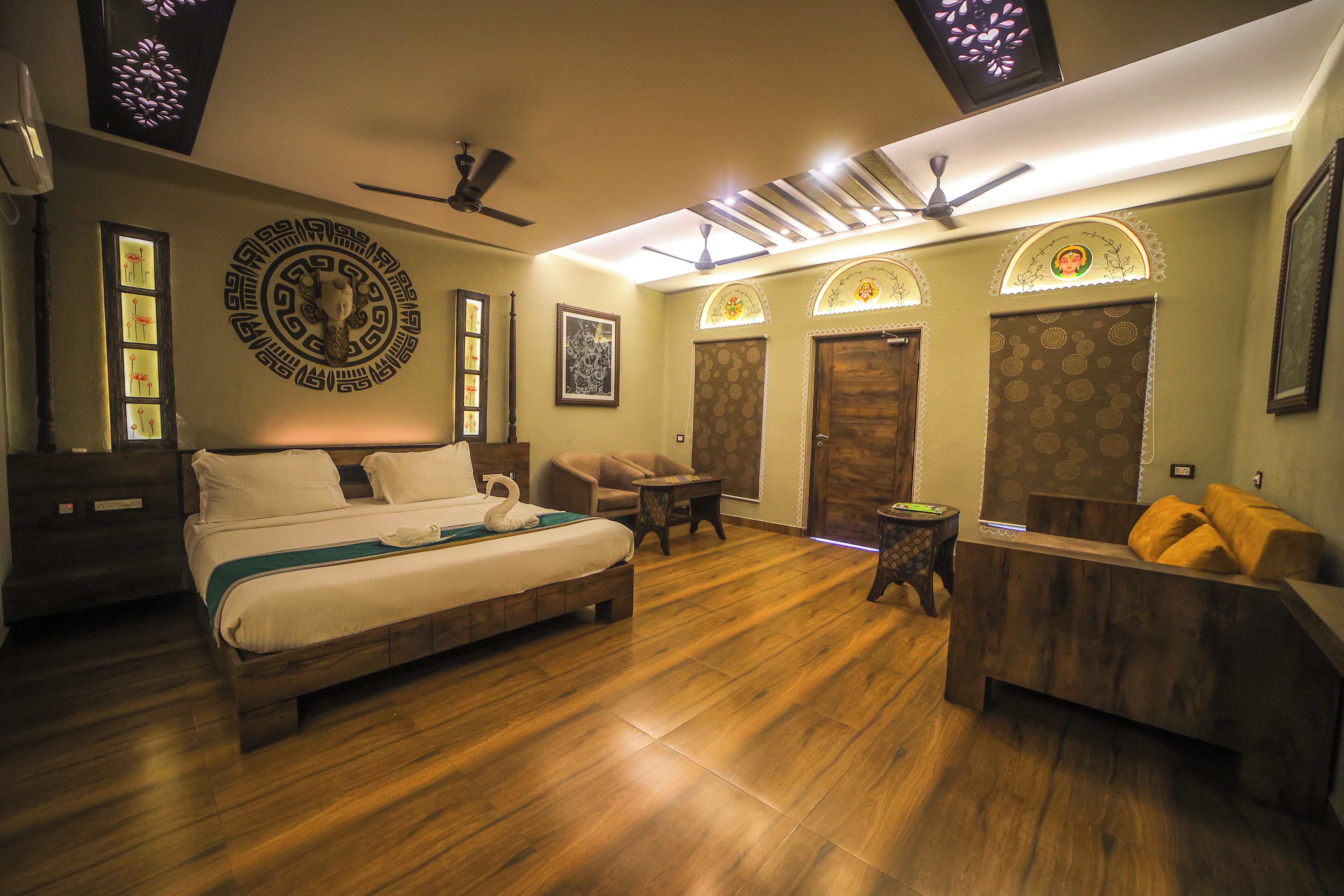 A hotel room with a bed, a seating area, a desk, and a door.