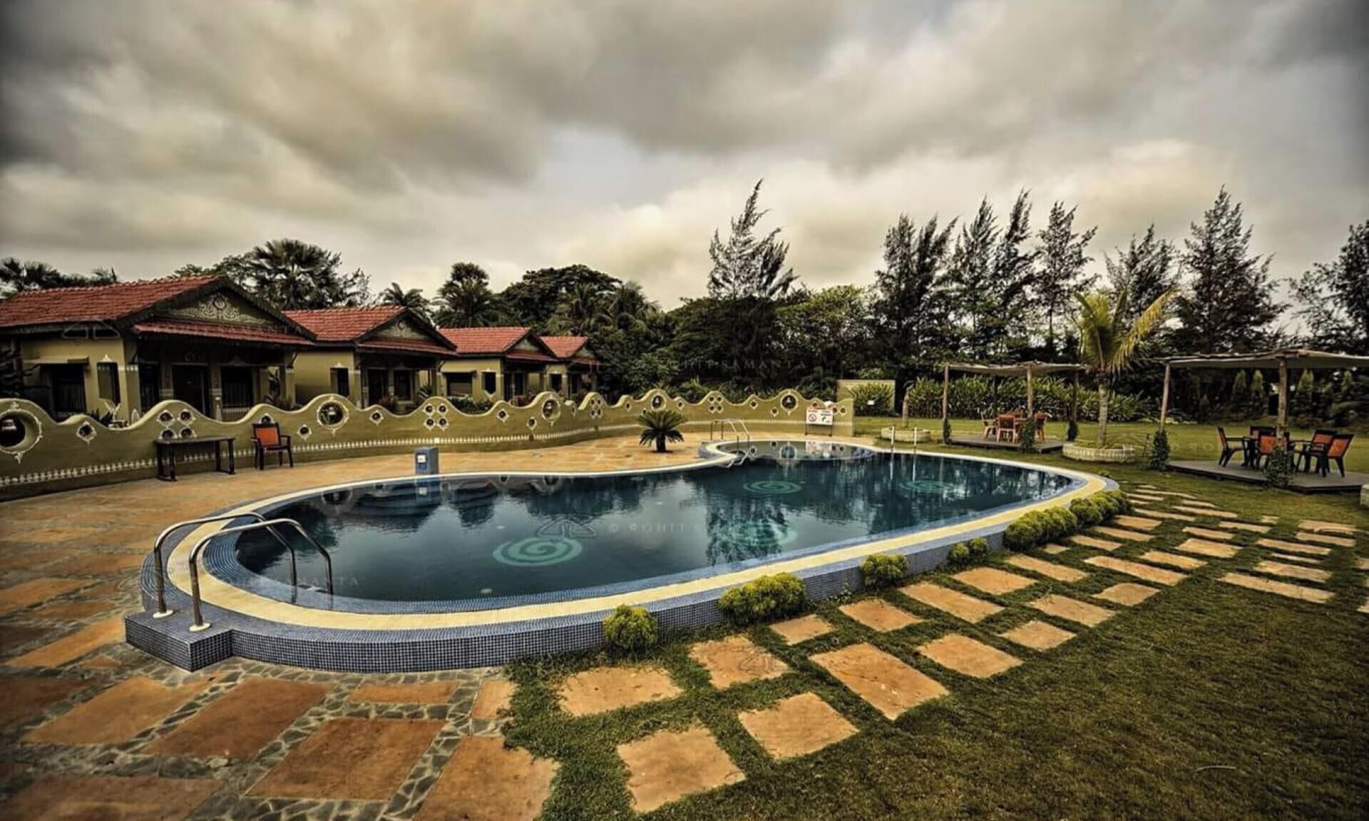 Una piscina con borde de azulejos, rodeada por un camino de piedra y un muro bajo.