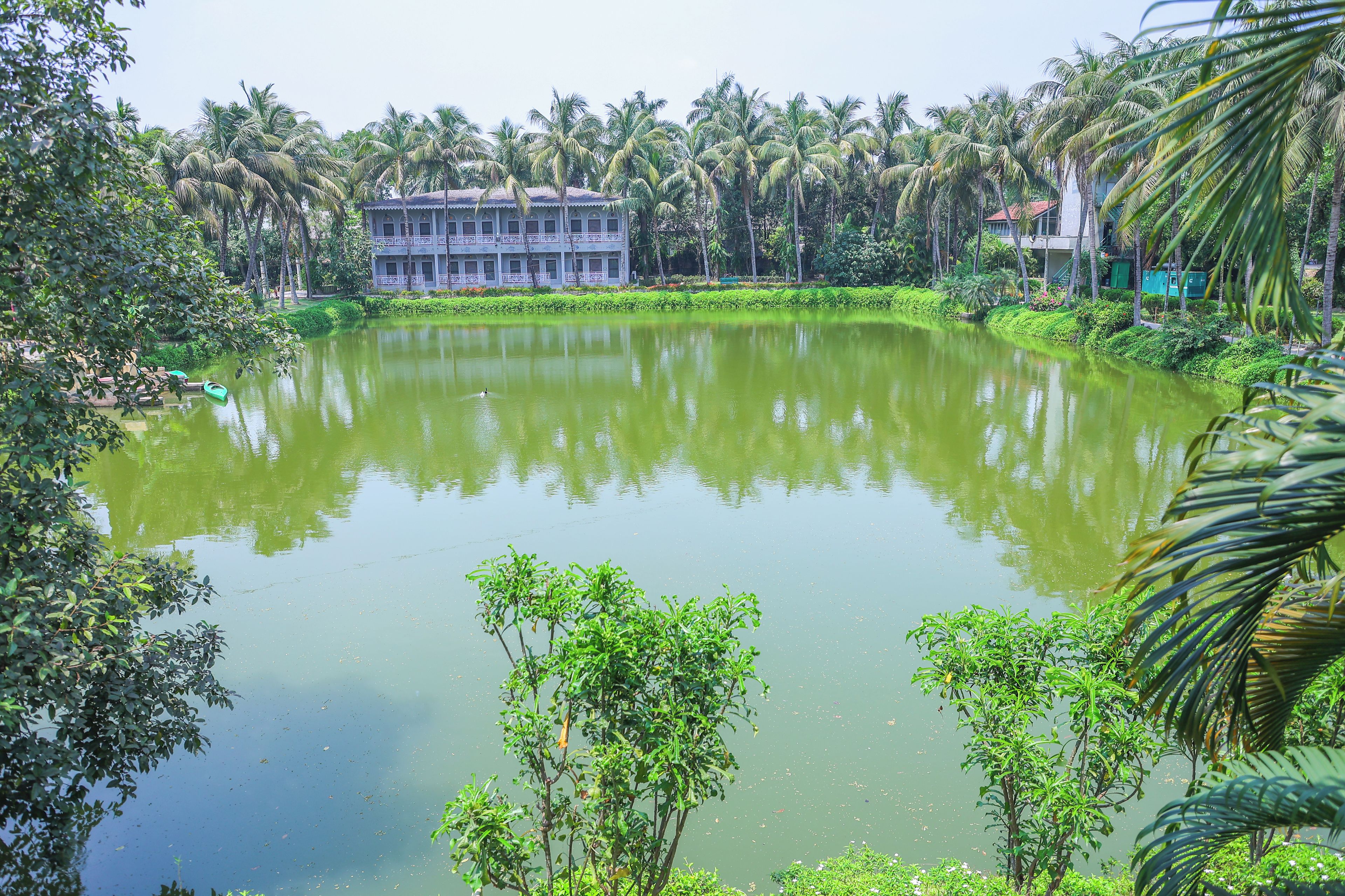 A calm lake surrounded by lush greenery and a building with multiple balconies.