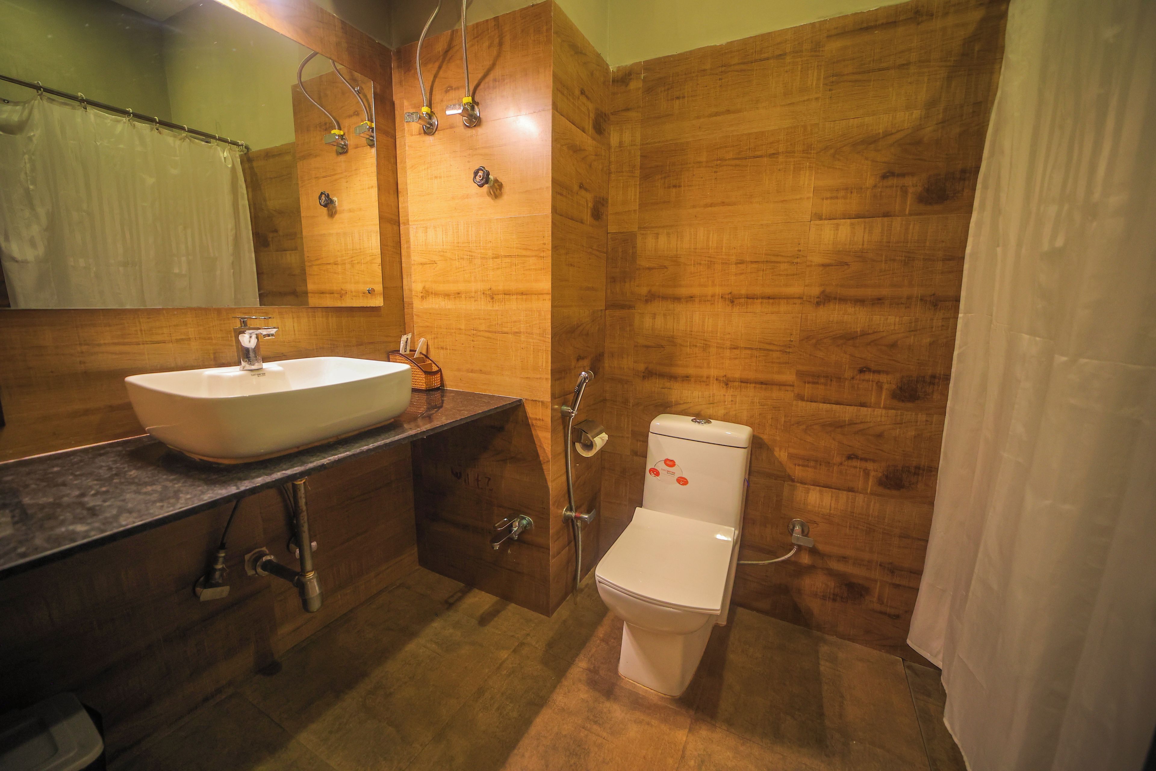 Un baño con pared de madera, un lavamanos blanco, un inodoro y una ducha.