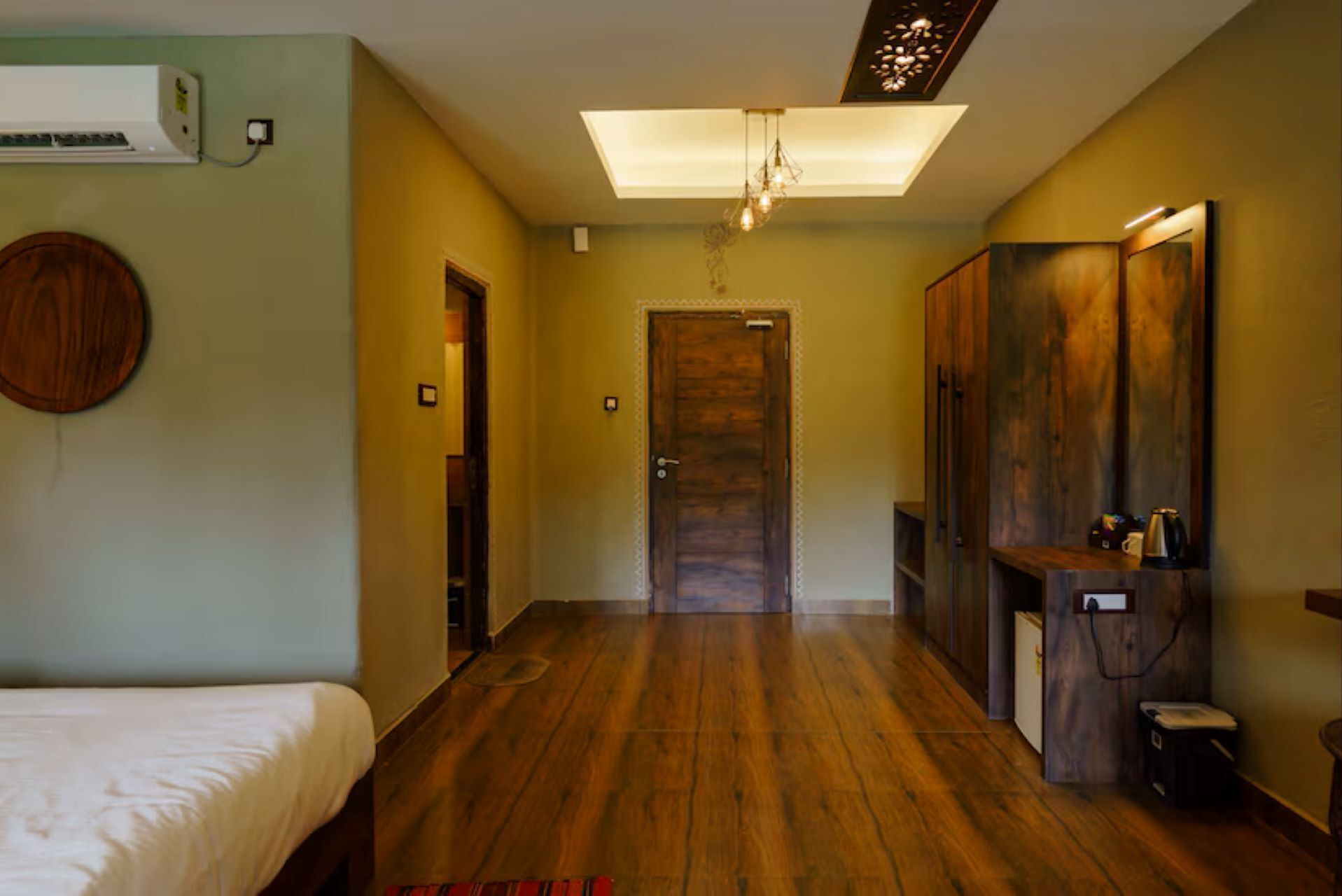 Une chambre d’hôtel avec un plancher en bois, un lit, un bureau avec une chaise, un miroir et une porte.