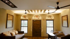 A room with a sofa, armchairs, a ceiling fan, a door with decorative arches, and a window with bars. - Breathing Earth (Diamond Harbour)