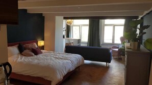 Een slaapkamer met een bed, een bureau en een stoel. Er is een raam met gordijnen en een plantje op het bureau.