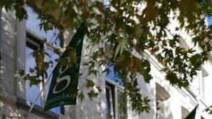 A building with a sign reading "Brenzelos" and a green flag with "B" on it. There are outdoor seating areas with tables and chairs.
