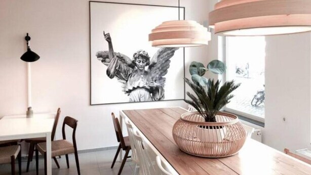 Een eetgedeelte met een houten tafel, stoelen, een groot kunstwerk in een lijst, een hanglamp en een potplant.