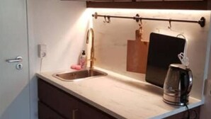 Een kleine keuken met een inbouwmagnetron, een roestvrijstalen spoelbak en een koffiezetapparaat.