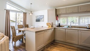 Een moderne keuken met een centraal kookeiland, houten vloeren en een eethoek met rieten meubels.