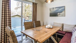 Een eetgedeelte met een houten tafel, rieten stoelen, een bank en een schilderij aan de muur.