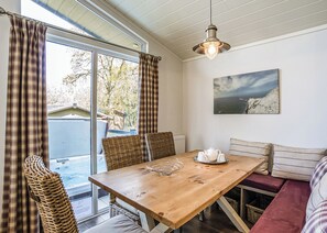 Un coin repas avec une table en bois, des chaises en osier, un banc et un tableau accroché au mur.
