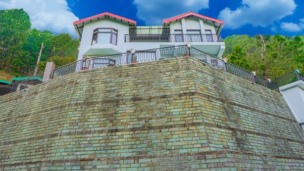 A two-story building with a red roof, a balcony, and a brick wall. - Kia Kasauli - 3 BHK, Villa with Kitchen+BonFire+Cook (Kasauli)