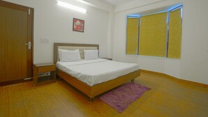 A bedroom with a wooden bed, a nightstand, a purple rug, a ceiling fan, and a window with yellow blinds. - Kia Kasauli - 3 BHK, Villa with Kitchen+BonFire+Cook (Kasauli)