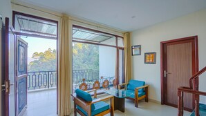 A room with a balcony, a wooden door, and a table with chairs. - Kia Kasauli - 3 BHK, Villa with Kitchen+BonFire+Cook (Kasauli)