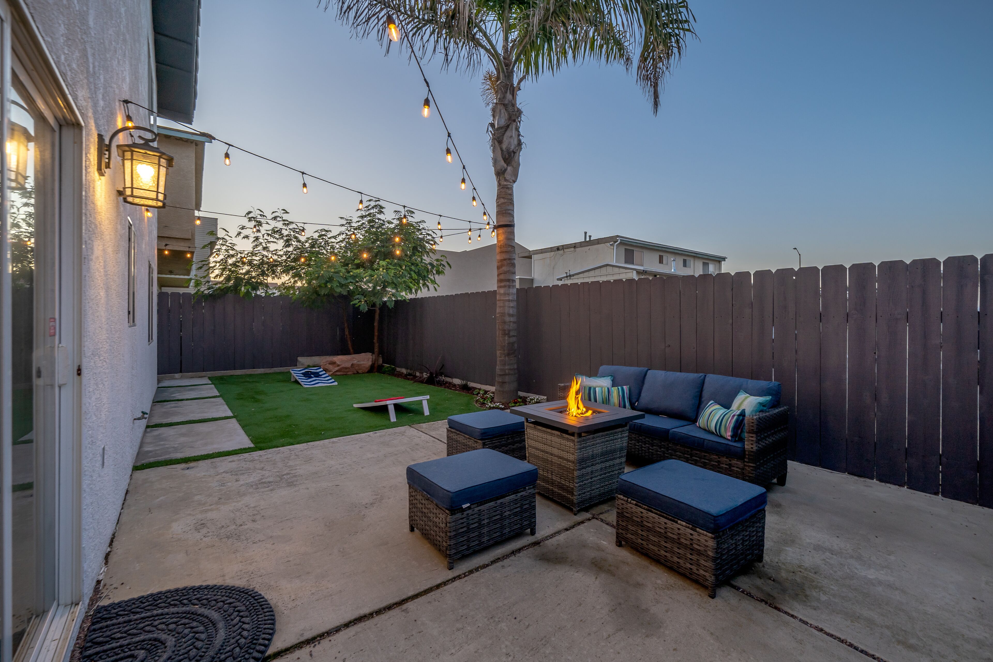 A backyard patio with outdoor furniture, a fire pit, and string lights.