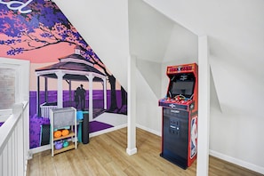 Une pièce comprenant un jeu d’arcade de basketball, une fresque représentant un kiosque et une petite étagère avec des ballons de sport.