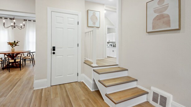 Una escalera con escalones de madera que conduce a un segundo piso, una puerta blanca y un comedor con una mesa y sillas.