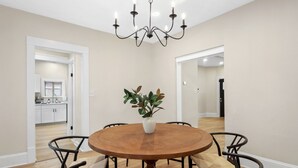 Un comedor con una mesa redonda de madera, cuatro sillas, un jarrón con plantas y una araña.