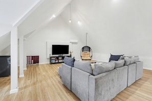 Un salon spacieux avec un canapé d’angle gris, un fauteuil suspendu et un téléviseur à écran plat.