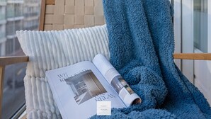 A magazine on a cushioned chair with a blue towel, a window with a view of buildings, and a label indicating 'Floor 1 Seaside.' - Comfort Floor, light and spacious at a top location (Knokke-Heist)