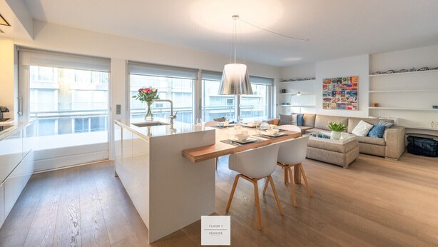 A modern kitchen with a central island, a dining area with chairs, a sofa, and a bookshelf. - Comfort Floor, light and spacious at a top location (Knokke-Heist)