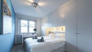 A modern bedroom with a bed, bedside tables, a radiator, a window, and a wardrobe. - Comfort Floor, light and spacious at a top location (Knokke-Heist)