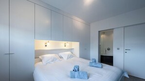 Ein modernes Schlafzimmer mit einem großen Bett, eingebautem Kleiderschrank und einer Duschkabine.