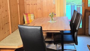 A wooden-paneled room with a wooden table, black leather chairs, a bench, and a view of a grassy field through a door. - Wonderful apartment with fantastic view Top 2 (2nd floor) (Wald am Arlberg)