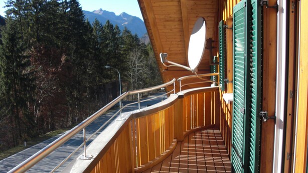 A wooden balcony with a metal railing, a view of a road, and a mountain in the background. - Wonderful apartment with fantastic view Top 2 (2nd floor) (Wald am Arlberg)