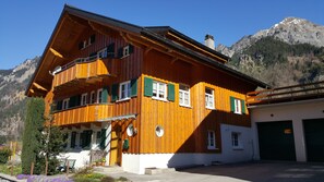 Un chalet de madera con balcón, garaje y montañas al fondo.
