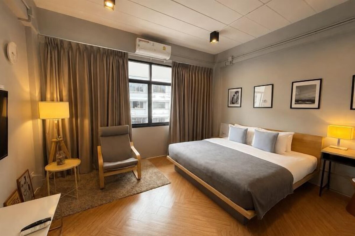 Een hotelkamer met een bed, een stoel, een bureau, een lamp en een raam met gordijnen.