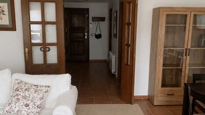 Una sala de estar con un sofá blanco, un sofá estampado, un aparador y una puerta que da a otra habitación.