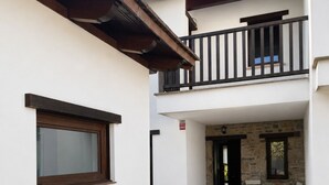 Un edificio de dos pisos con un balcón, una pared de piedra y un patio con mobiliario exterior.