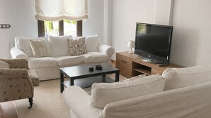 Una sala de estar con un sofá, una mesa de centro, un televisor y una ventana con cortinas.