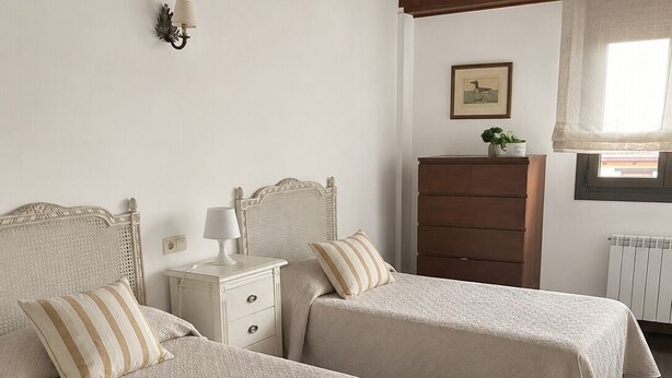 Una habitación con dos camas, una mesita de noche, un aparador, una lámpara de pared y un cuadro enmarcado.