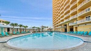 Zona de piscina de hotel con una pileta grande, camastros y un edificio de varios pisos con balcones.